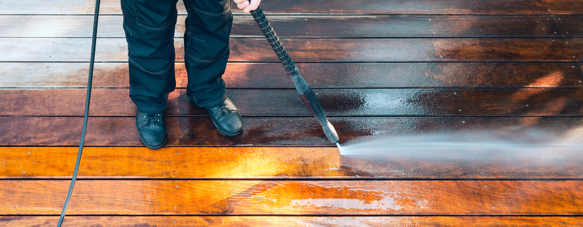 individual using pressure washer on wood deck