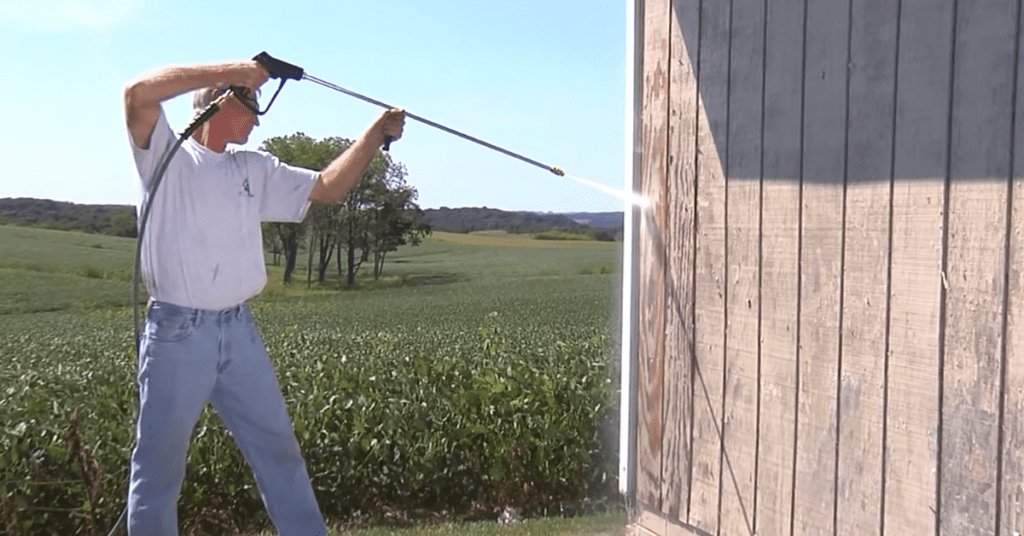 man using pressure washer on wood slat wall